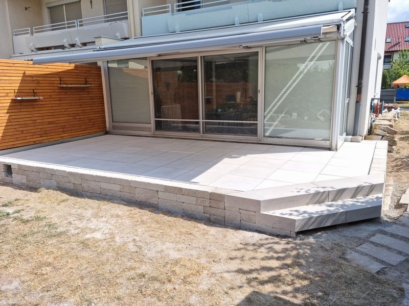 Eine steinerne Stützmauer stützt einen grasbewachsenen Hang, davor verläuft ein Kopfsteinpflasterweg.