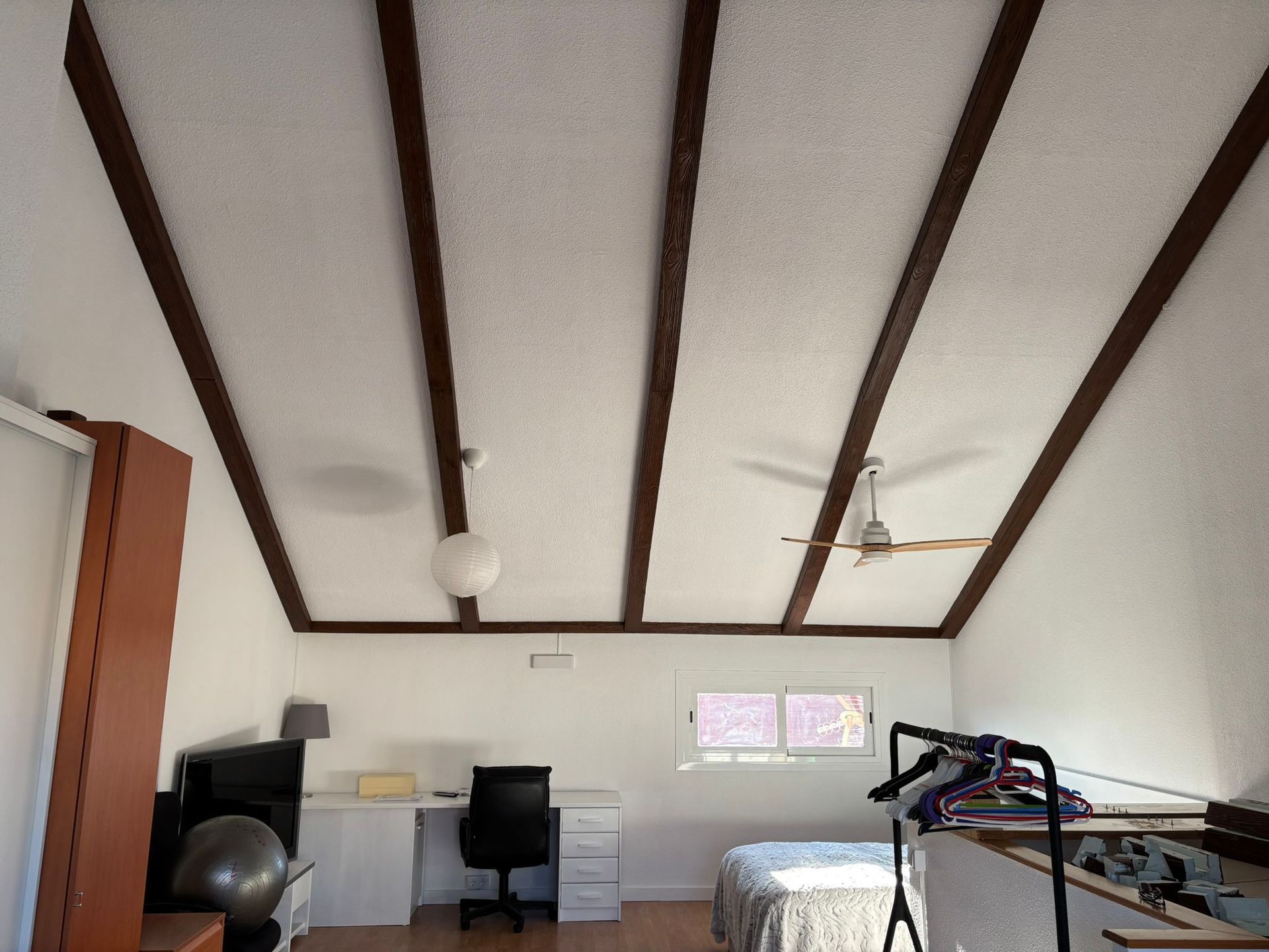 Un dormitorio con una cama, un escritorio y un ventilador de techo.