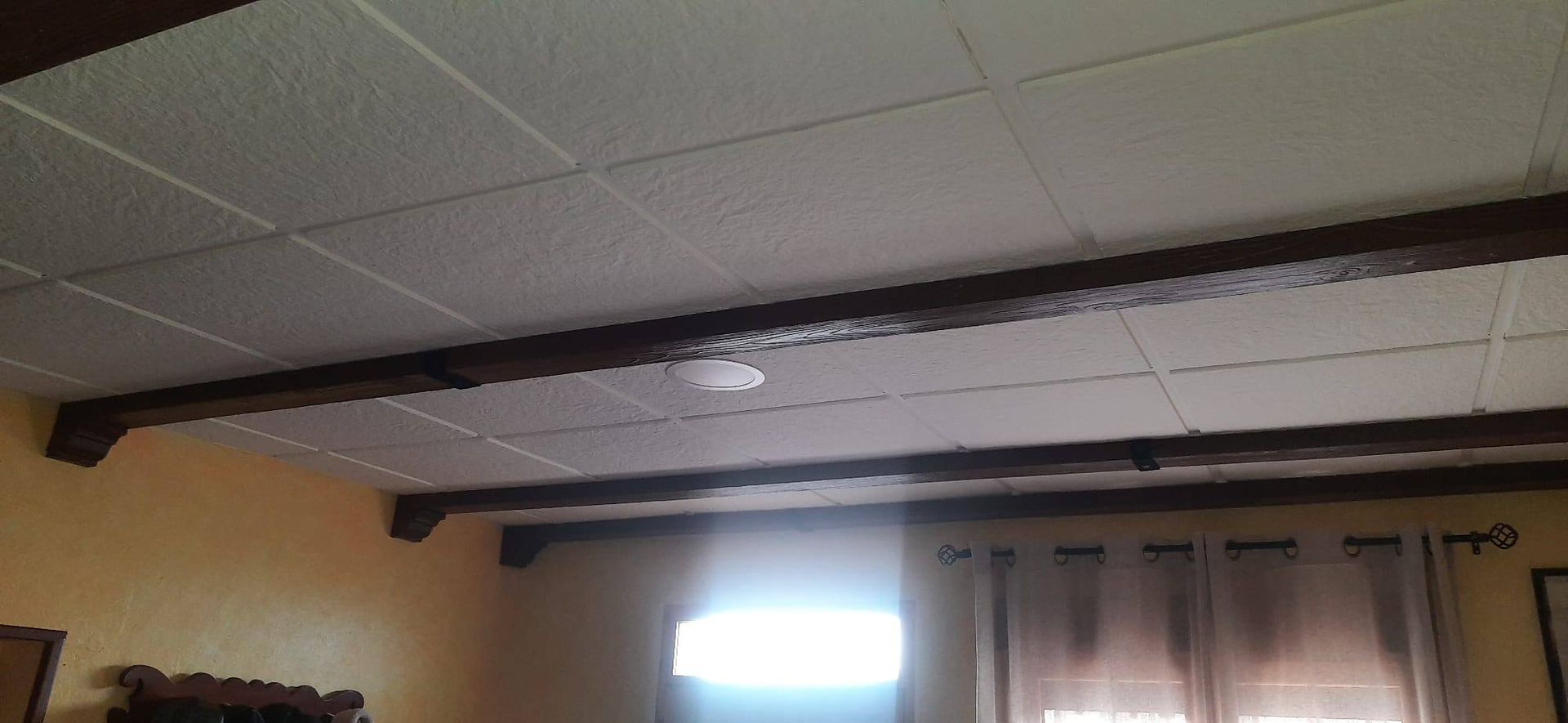 Un dormitorio con techo blanco y vigas de madera.