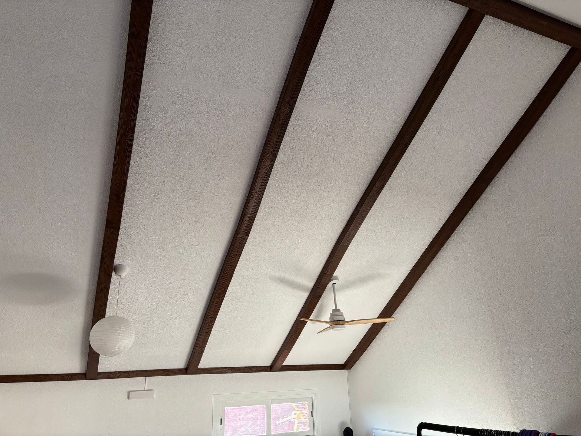 Un techo blanco con vigas de madera y un ventilador de techo.