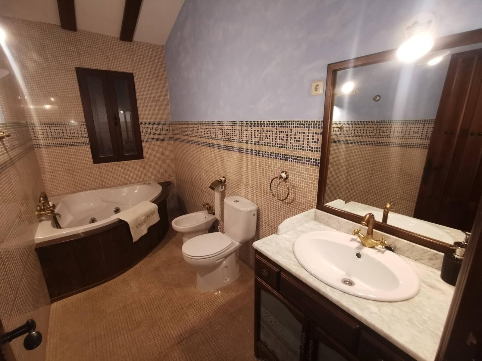 Baño con bañera, inodoro y lavabo de mármol en tonos beige cálidos.