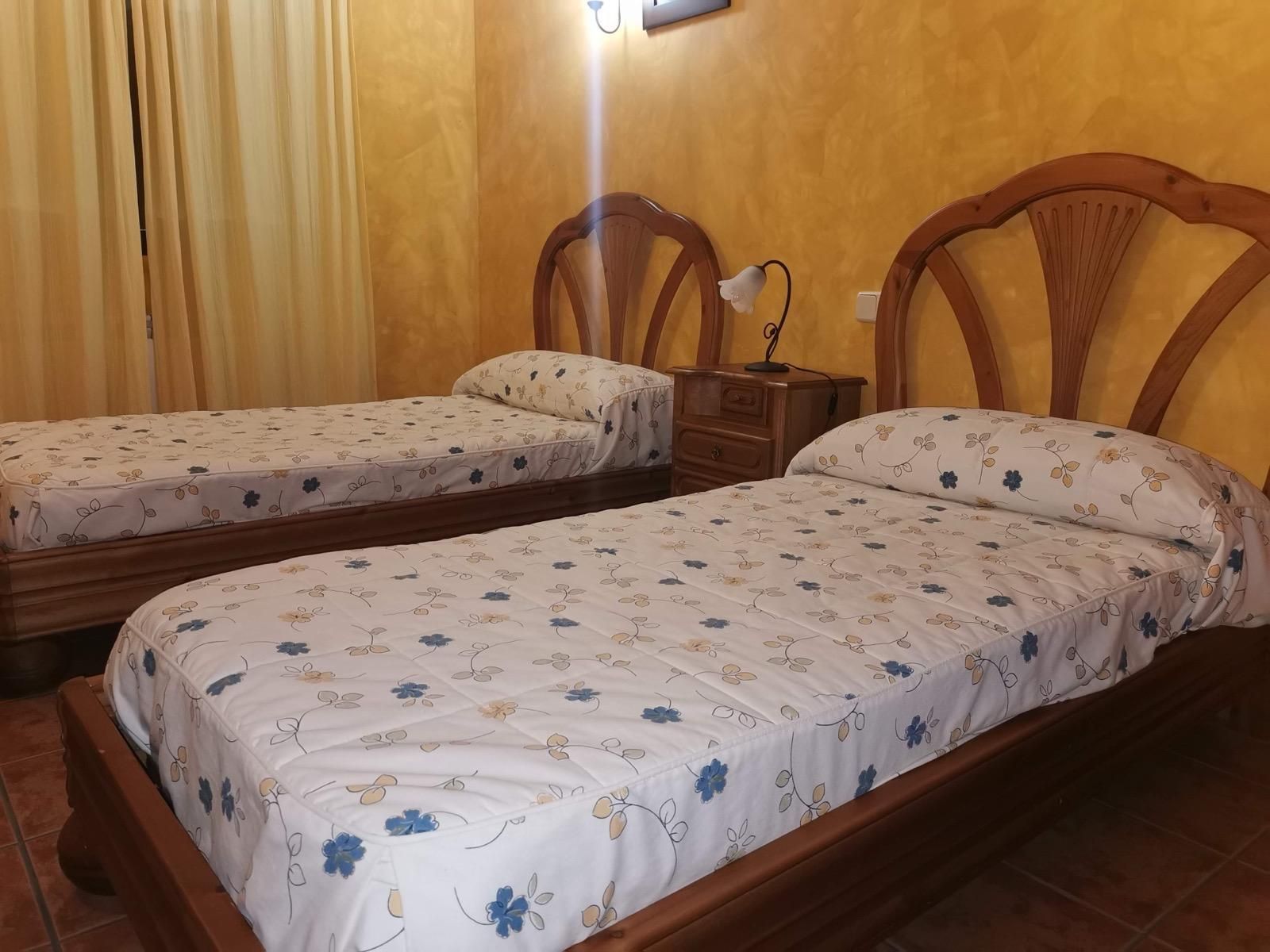Dos camas individuales con ropa de cama blanca estampada en un dormitorio con paneles de madera.