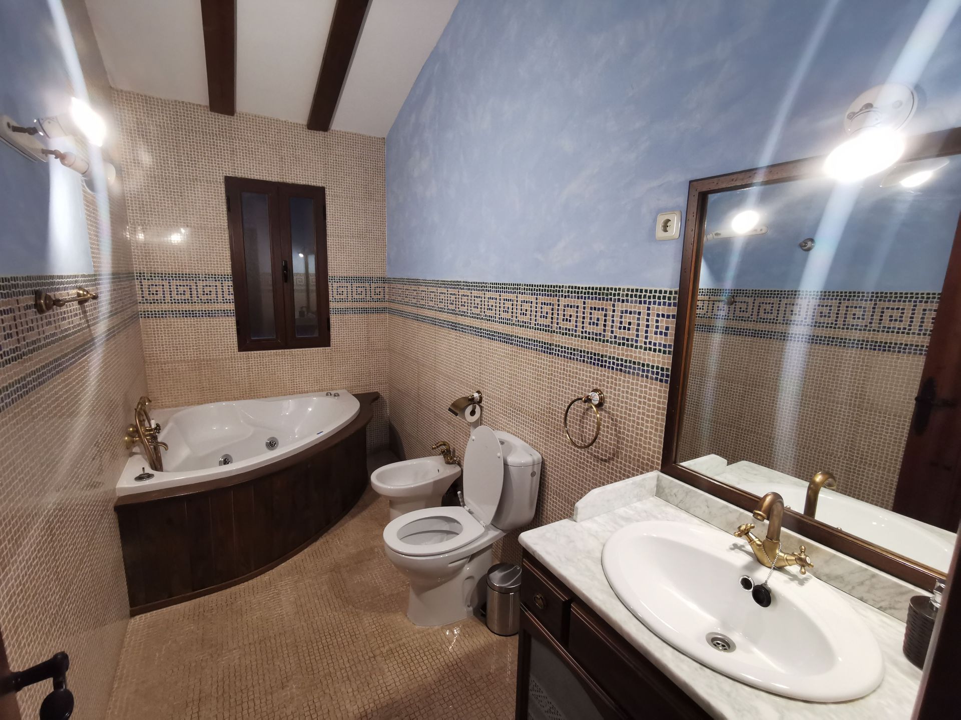 Baño con jacuzzi, inodoro, bidé y lavabo. Paredes alicatadas con detalles en azul y crema.