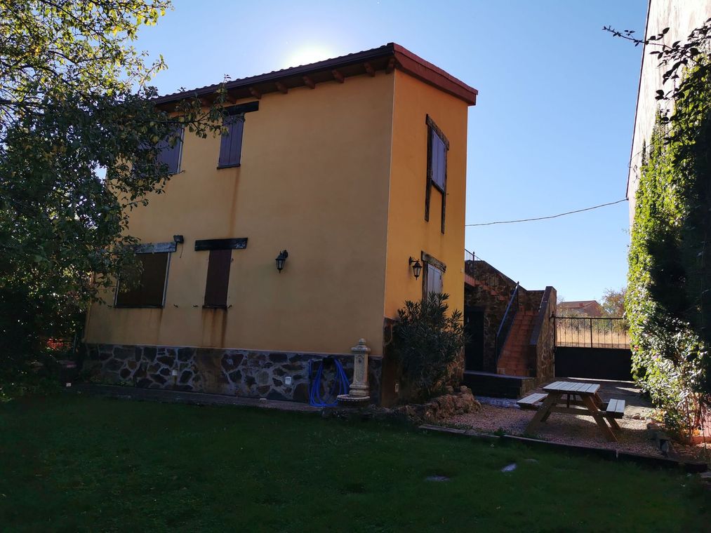 Casa amarilla con molduras blancas, porche y jardín. Árboles verdes al fondo.