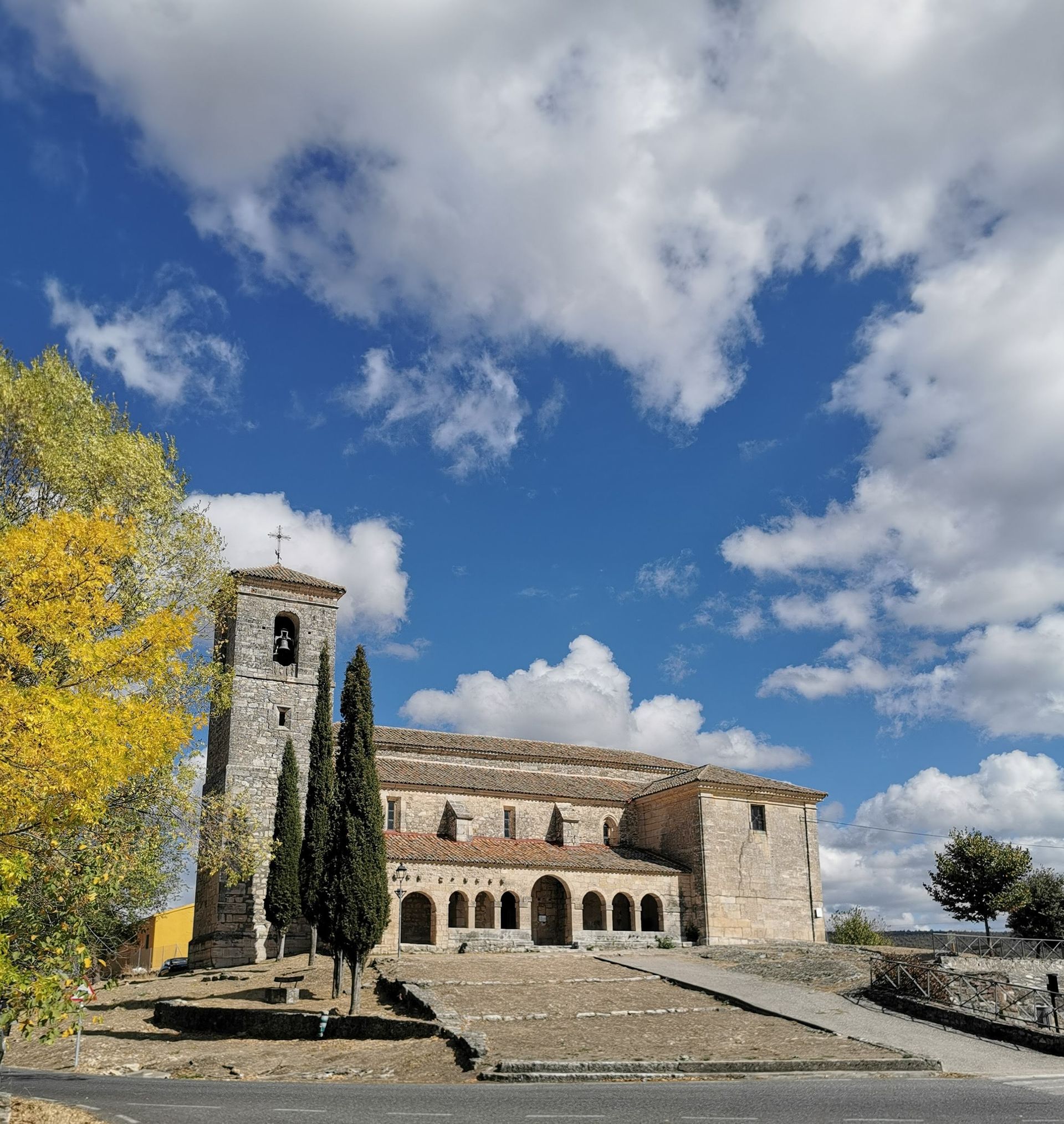 Iglesia de piedra con campanario bajo un cielo azul parcialmente nublado.