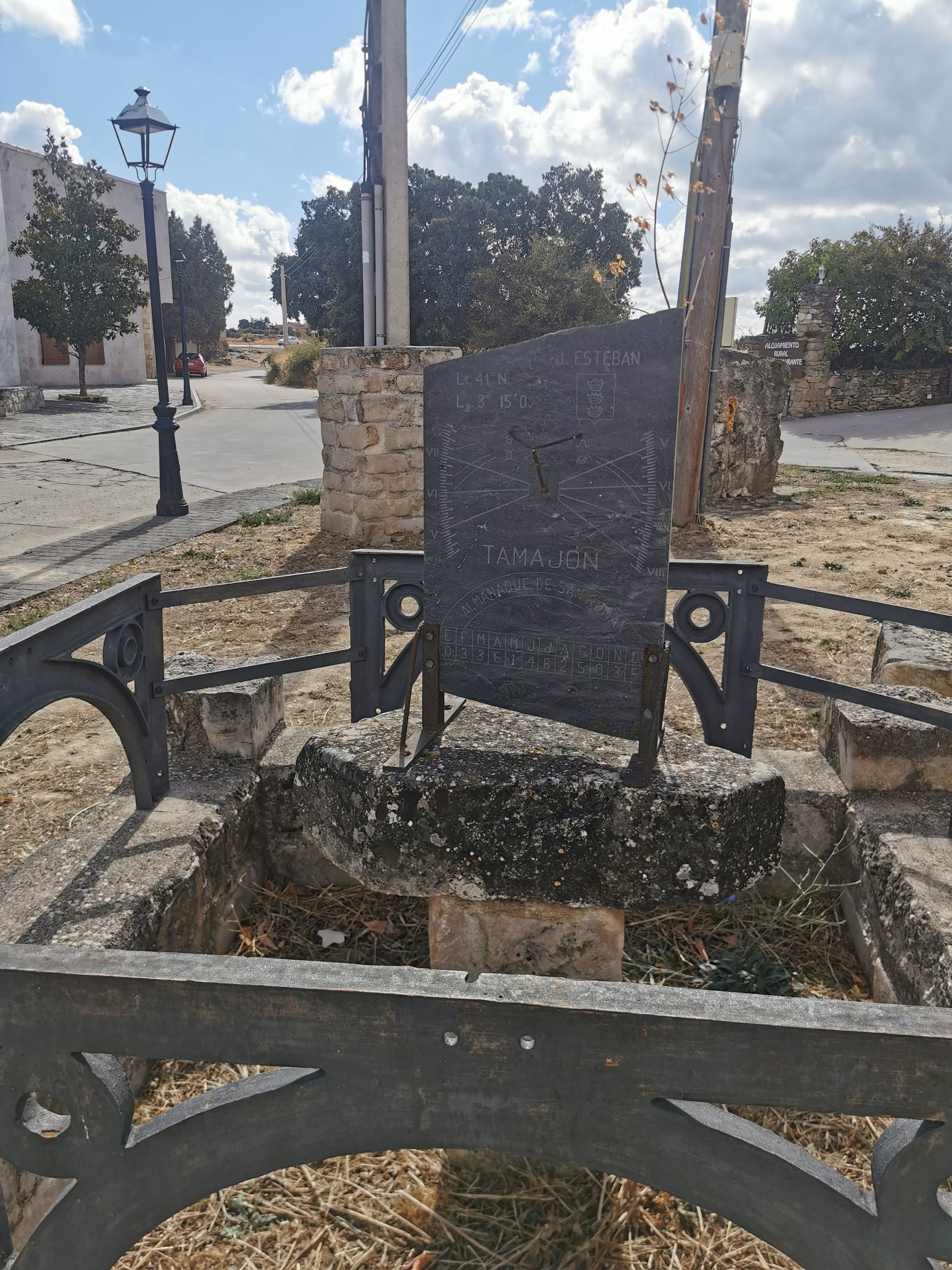 Un monumento de piedra desgastada detrás de una valla de hierro forjado, en una plaza de la ciudad.
