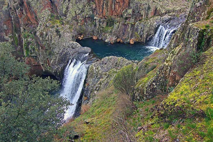 Dos cascadas caen en una piscina turquesa, rodeada de acantilados rocosos y vegetación verde.