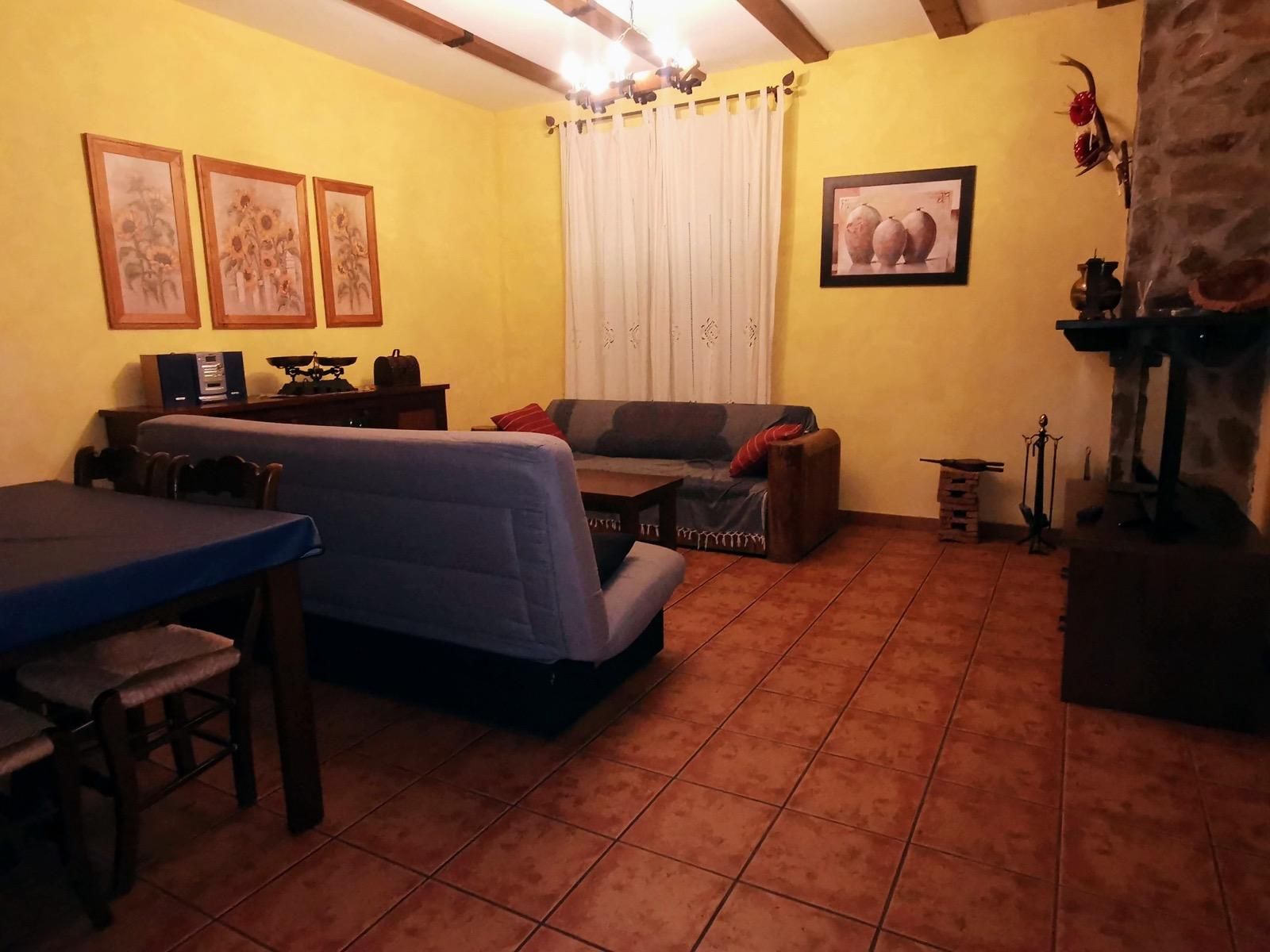 Acogedora sala de estar con paredes amarillas, sofá azul, suelo de baldosas, cortinas y cuadros enmarcados en las paredes.