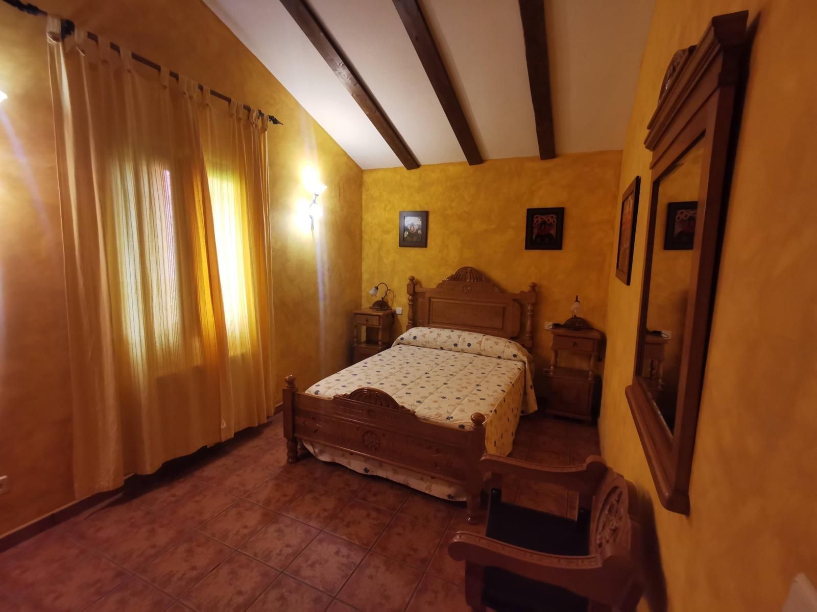Habitación acogedora con cama de madera, paredes de color amarillo cálido, cortinas y vigas de techo a la vista.