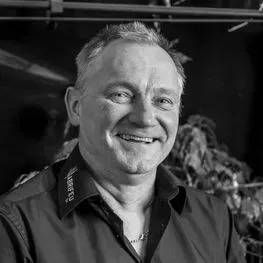 Homme souriant en chemise sombre, portrait en noir et blanc en intérieur