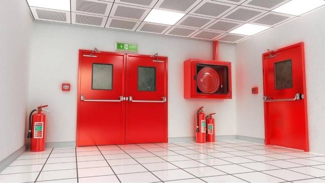 Portes de sortie de secours rouges dans un couloir blanc éclatant, avec extincteurs et dévidoir mural.