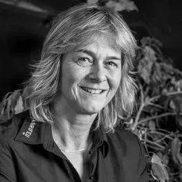 Portrait en noir et blanc d'une personne souriante aux cheveux mi-longs, en extérieur