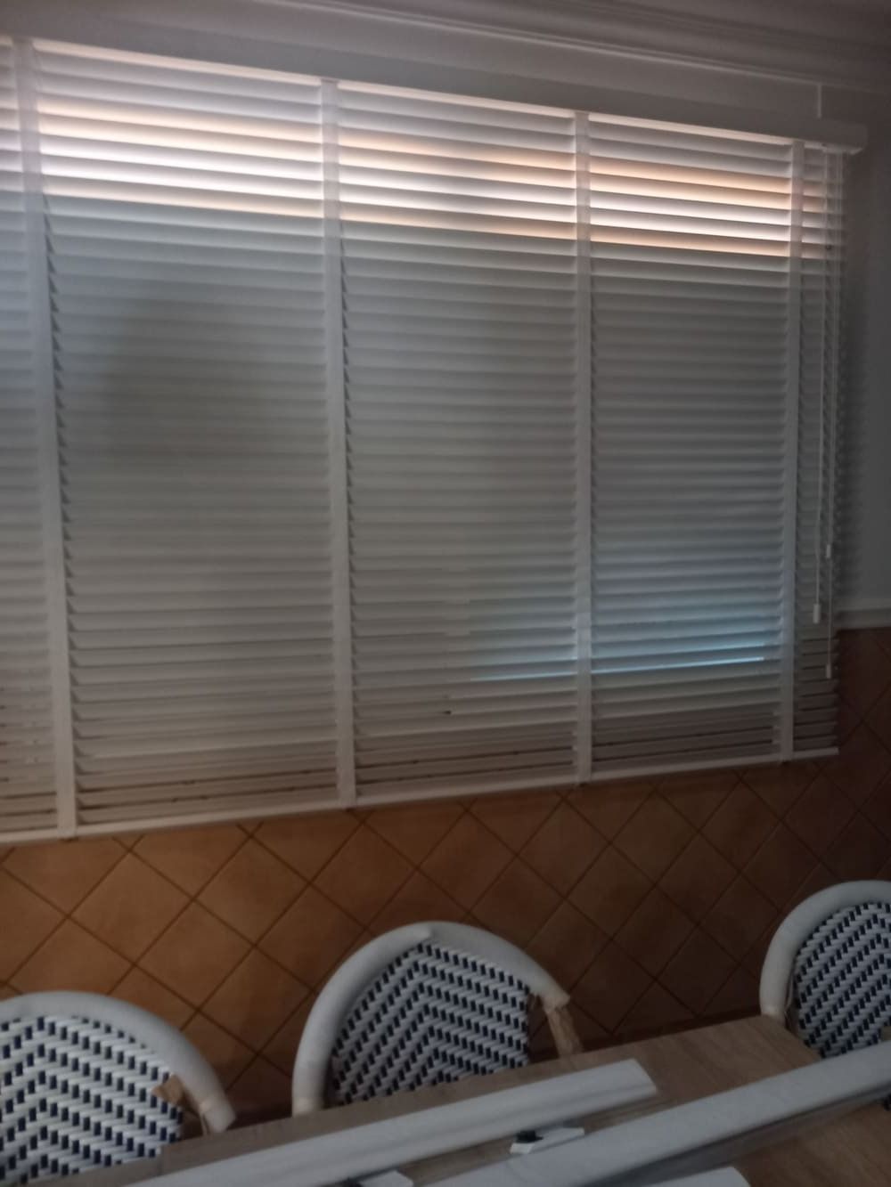 Una habitación con una mesa y sillas y una ventana con persianas.