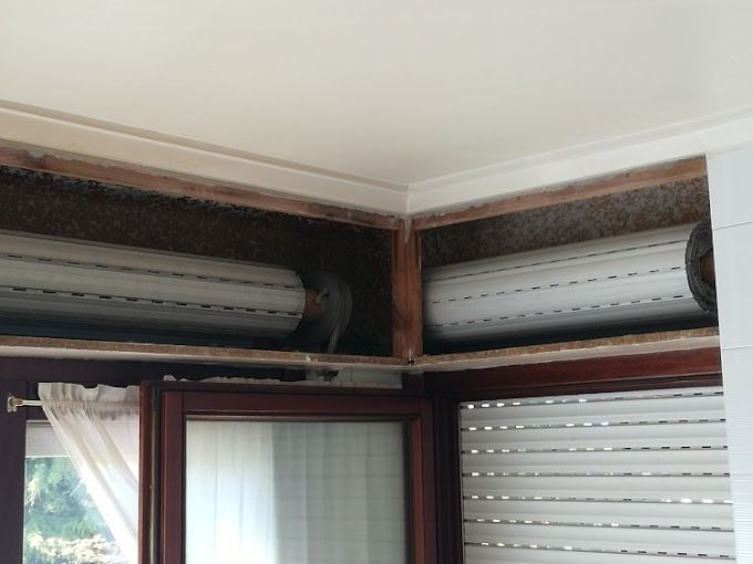 Un rincón de una habitación con una ventana y contraventanas.