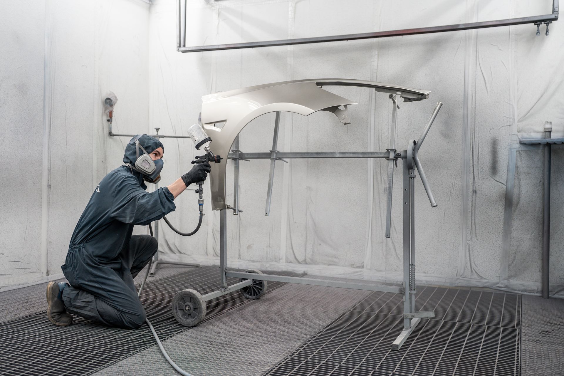 Ein Mann bemalt in einer Lackierkabine ein Auto mit Sprühfarbe.