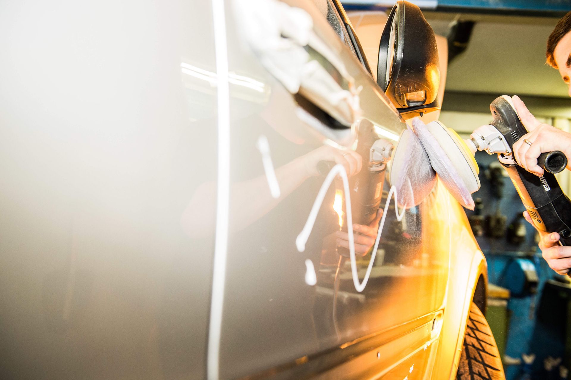 Ein Mann poliert in einer Garage ein Auto mit einer Maschine.