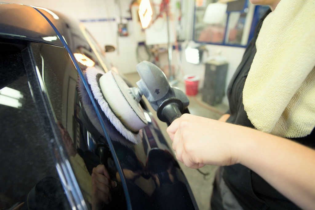 Eine Frau poliert in einer Garage ein Auto mit einer Maschine.