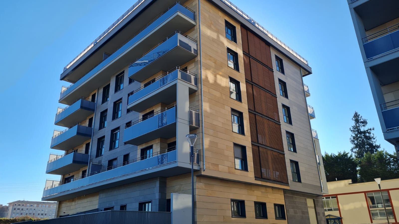 Un gran edificio de apartamentos con balcones azules y un cielo azul al fondo.