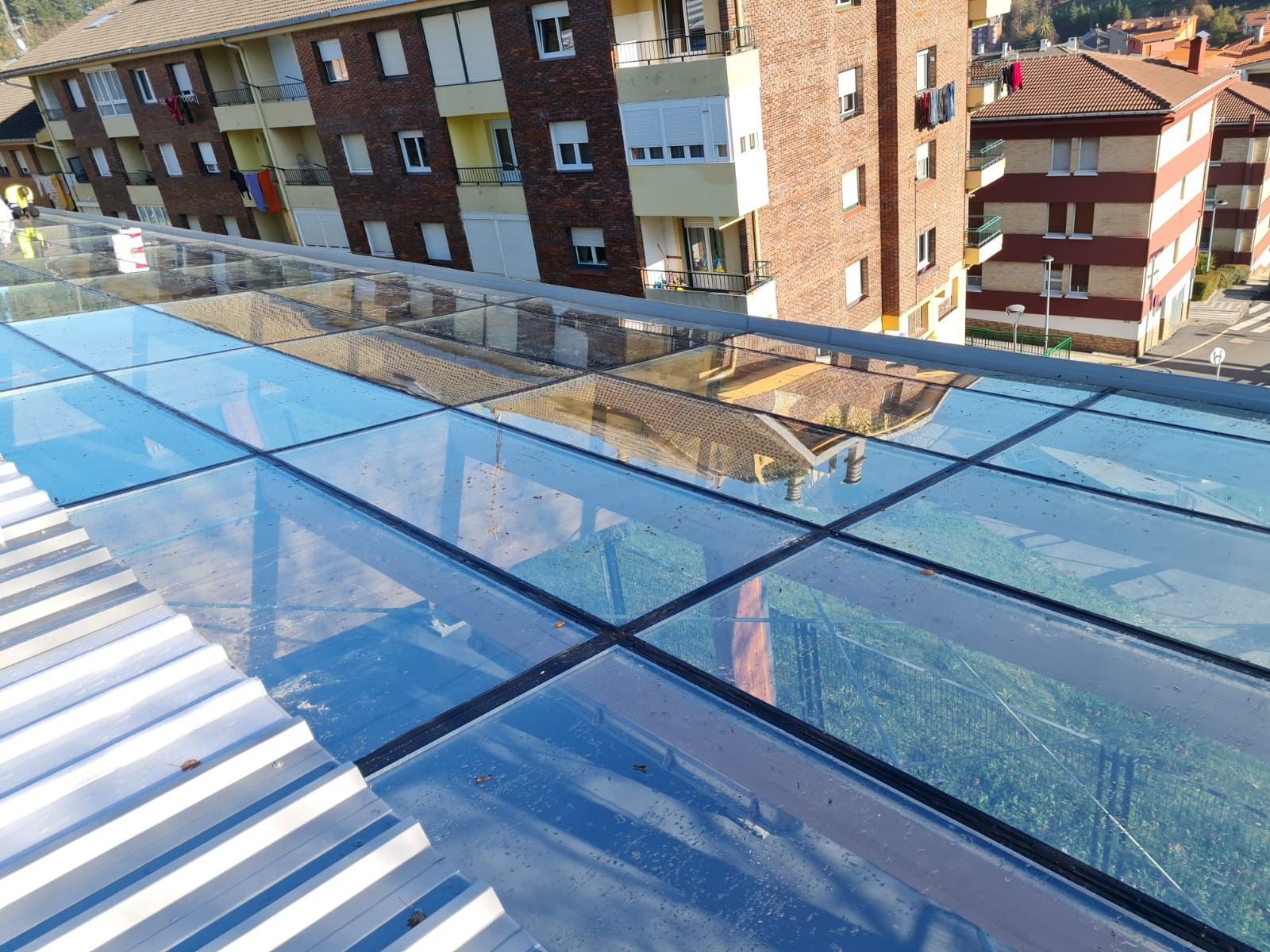 Un balcón con techo de cristal y edificios de ladrillo al fondo.