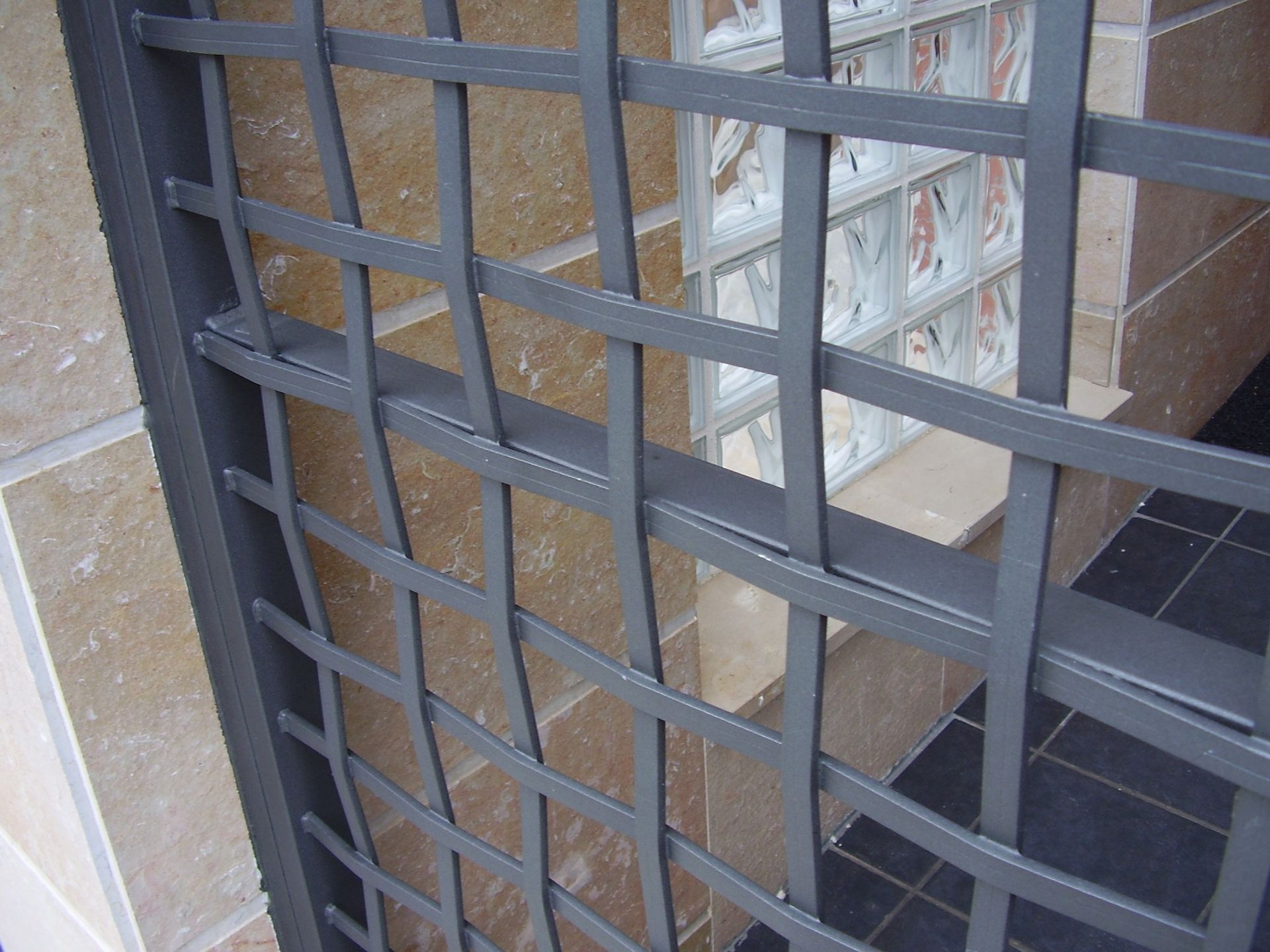 Un primer plano de una valla metálica con una pared de ladrillos al fondo.