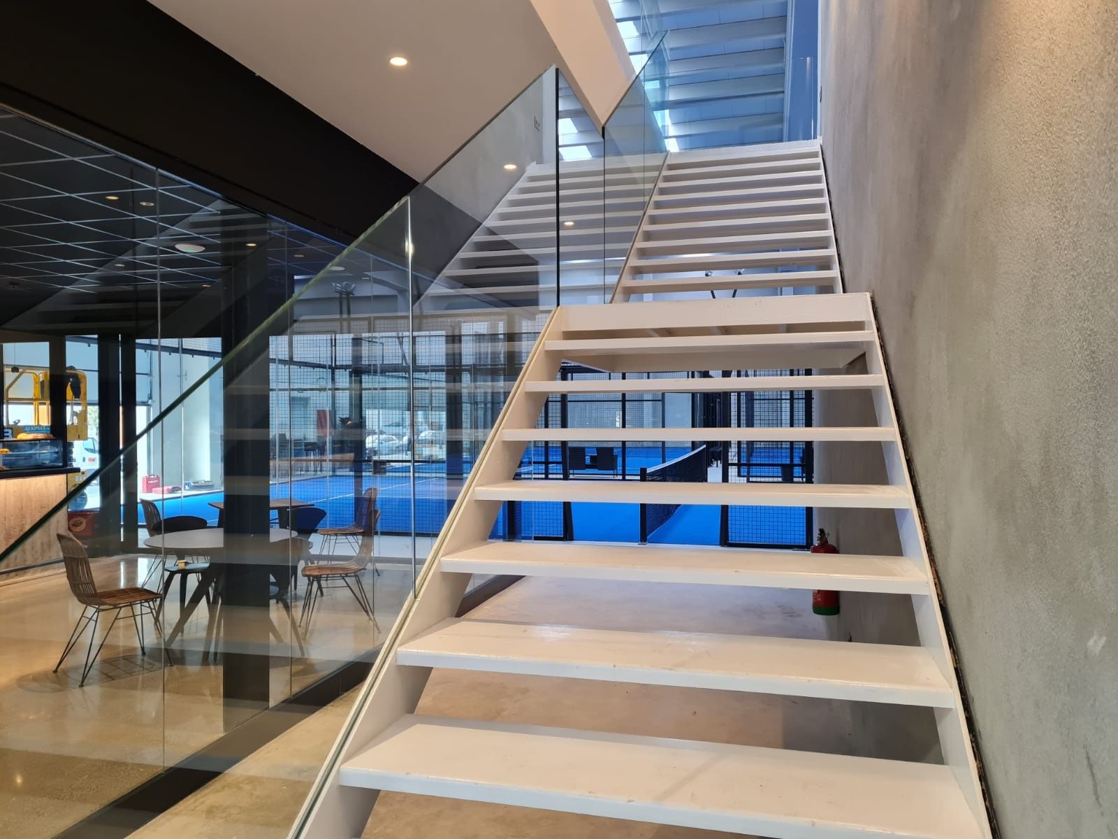 Una escalera blanca con barandilla de cristal en un edificio.