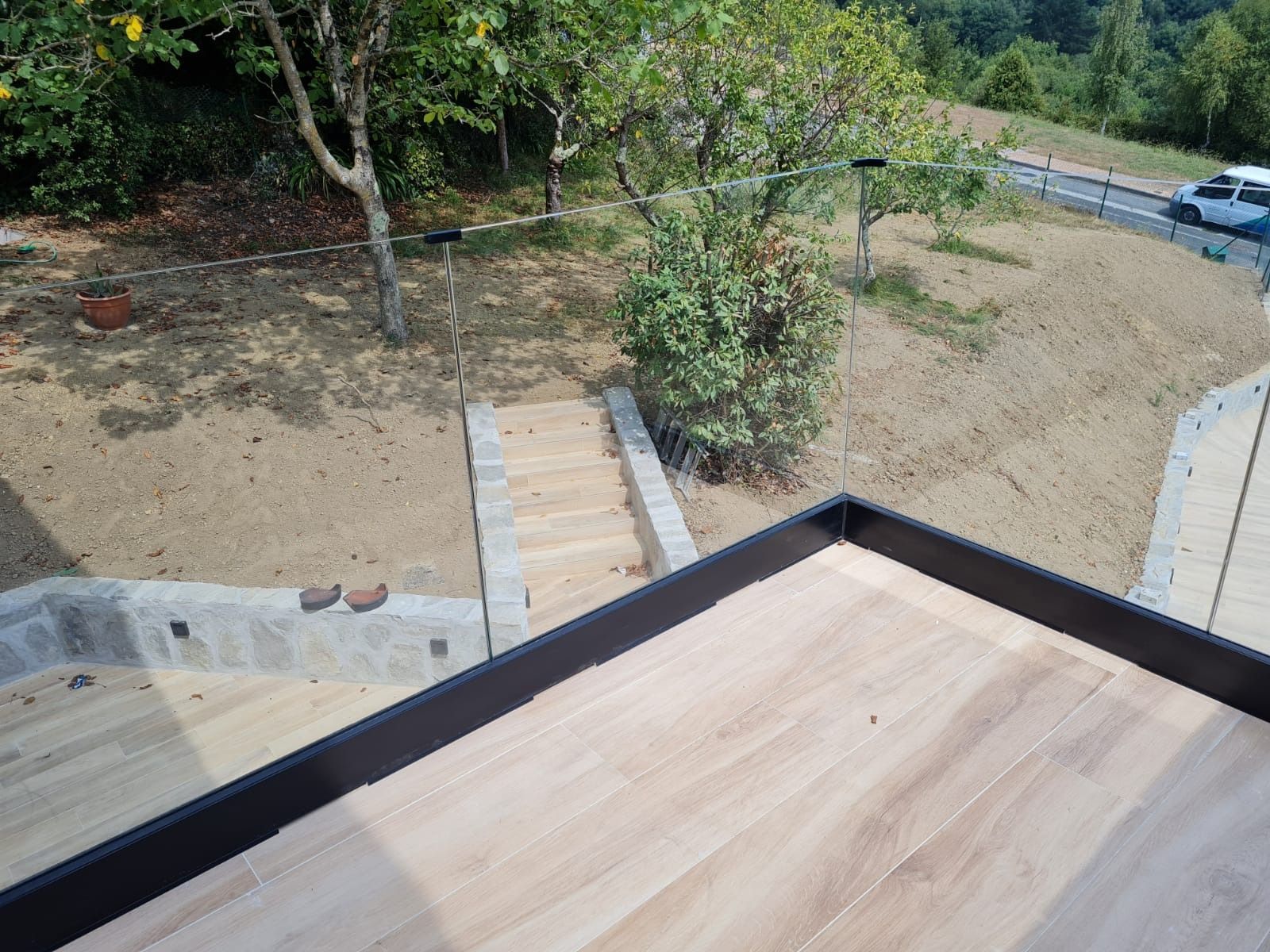 Una terraza de madera con barandilla de cristal y escaleras al fondo.