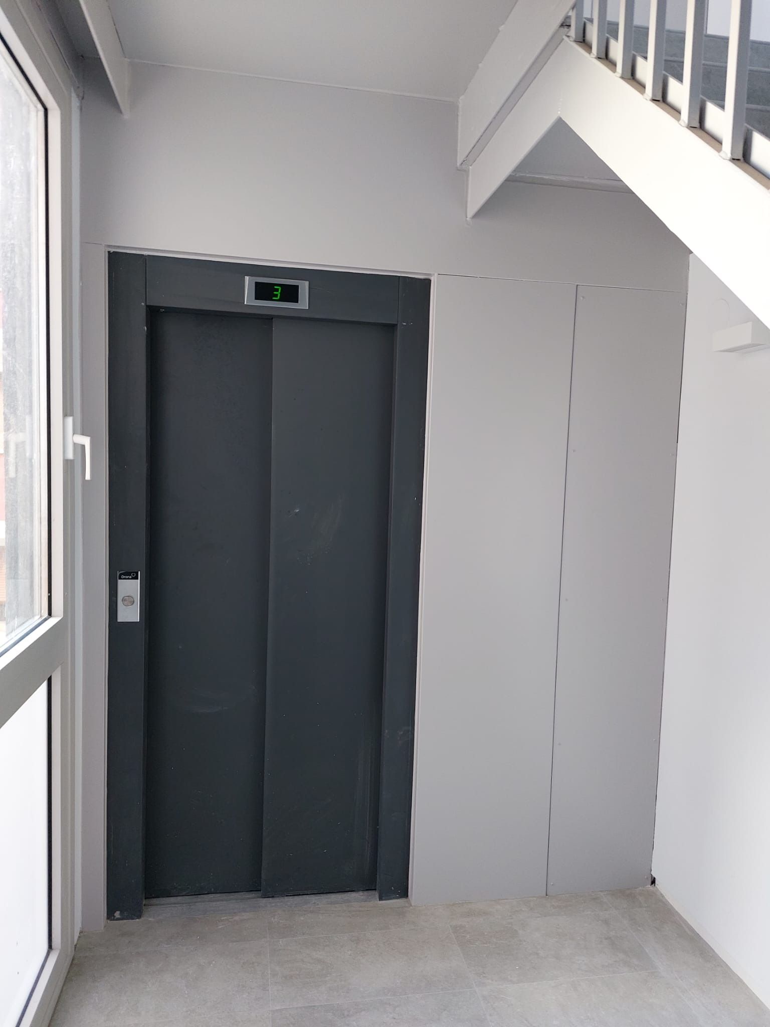 Un ascensor está en un pasillo al lado de una escalera.