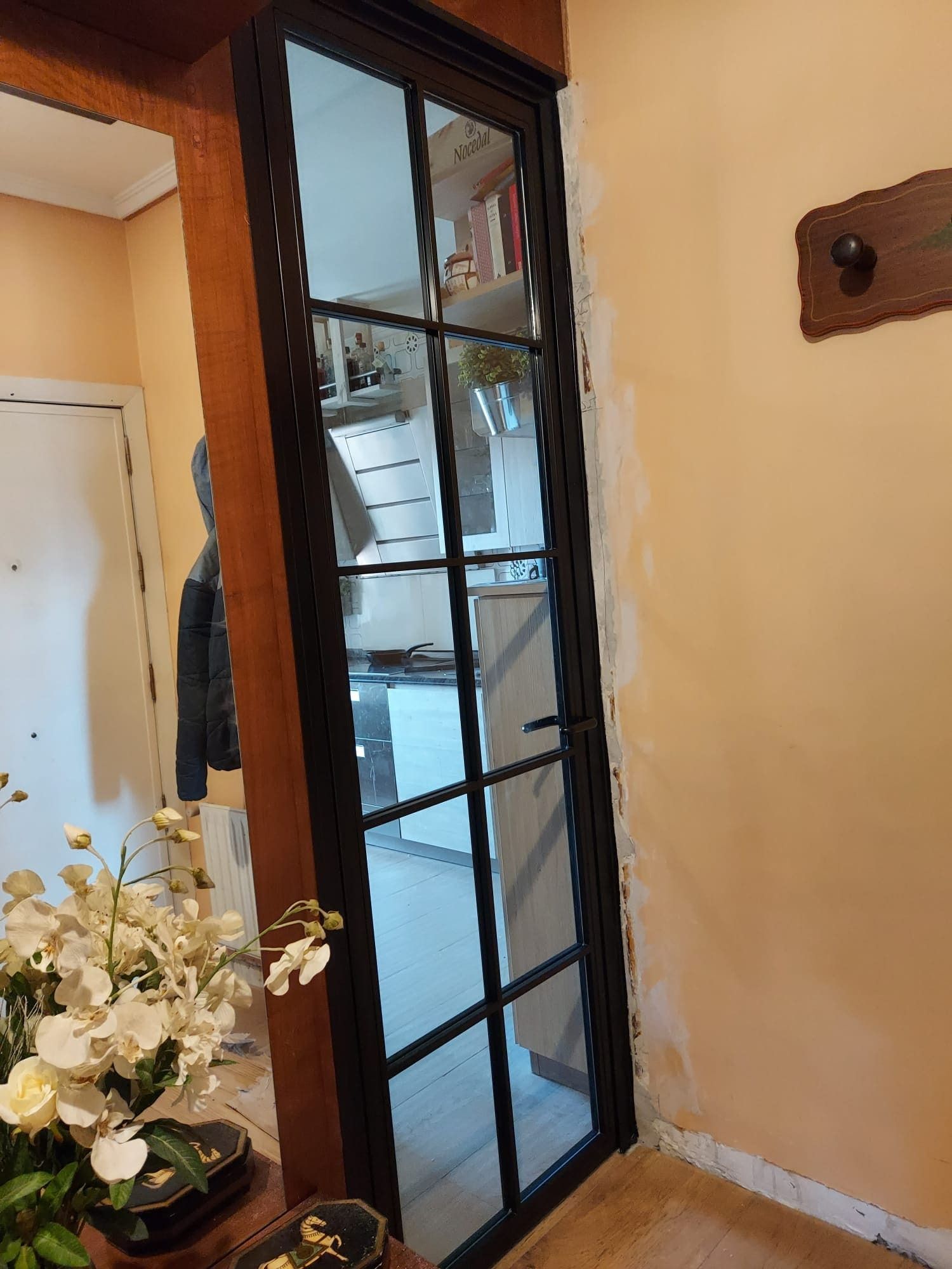 Una habitación con una puerta de cristal y un jarrón de flores sobre una mesa.