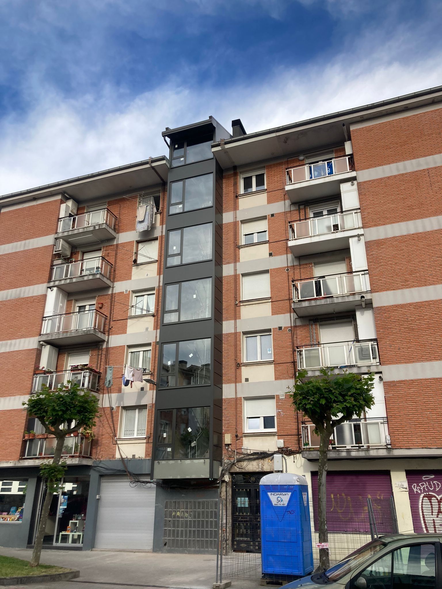 Un edificio de ladrillo con un baño portátil azul enfrente.