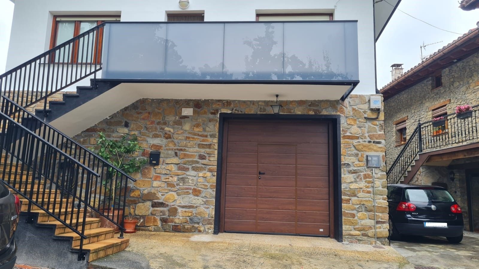 Un coche está aparcado delante de una casa con escaleras y puerta de garaje.