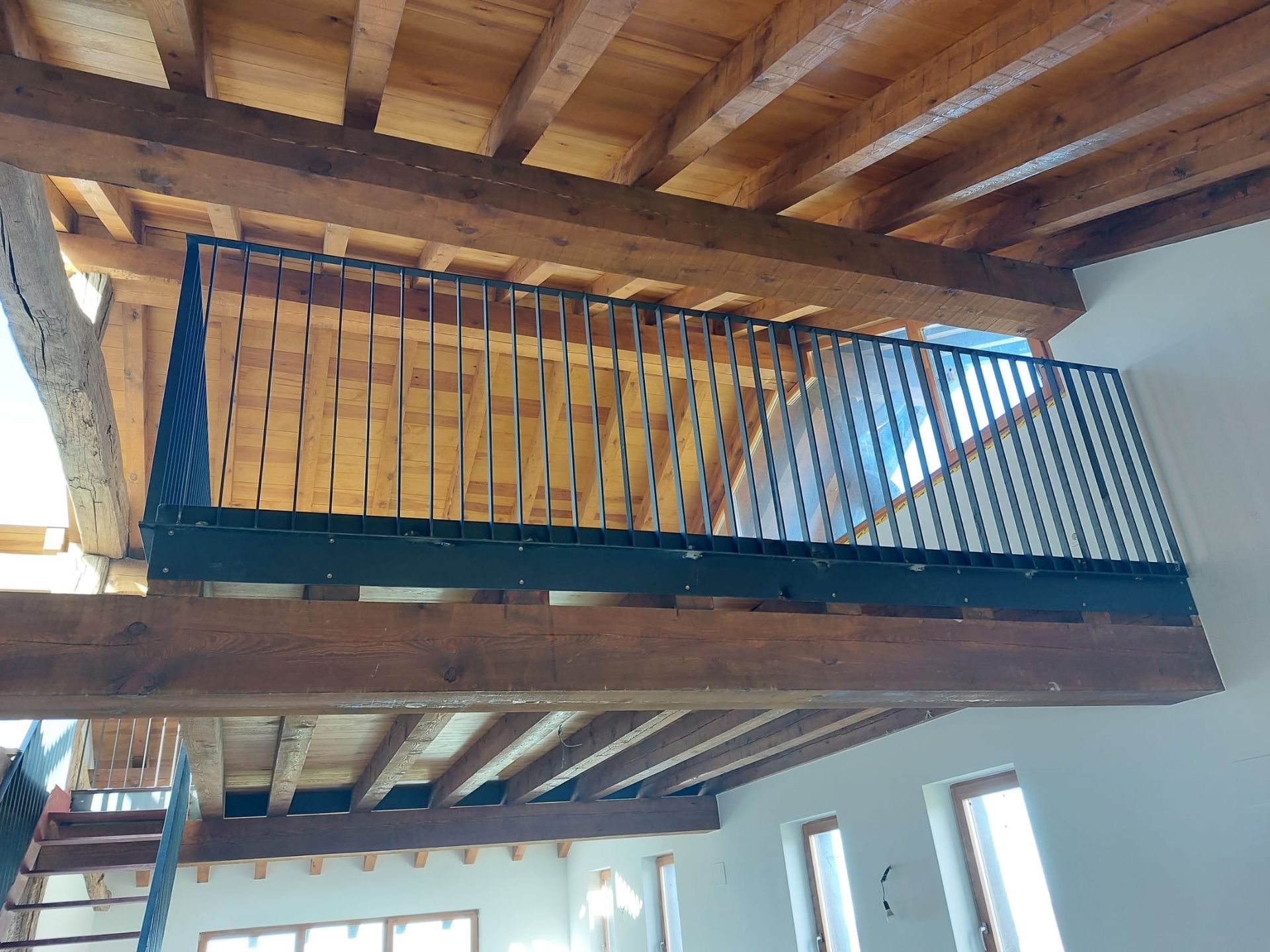 Un balcón con barandilla de metal en una habitación con vigas de madera.