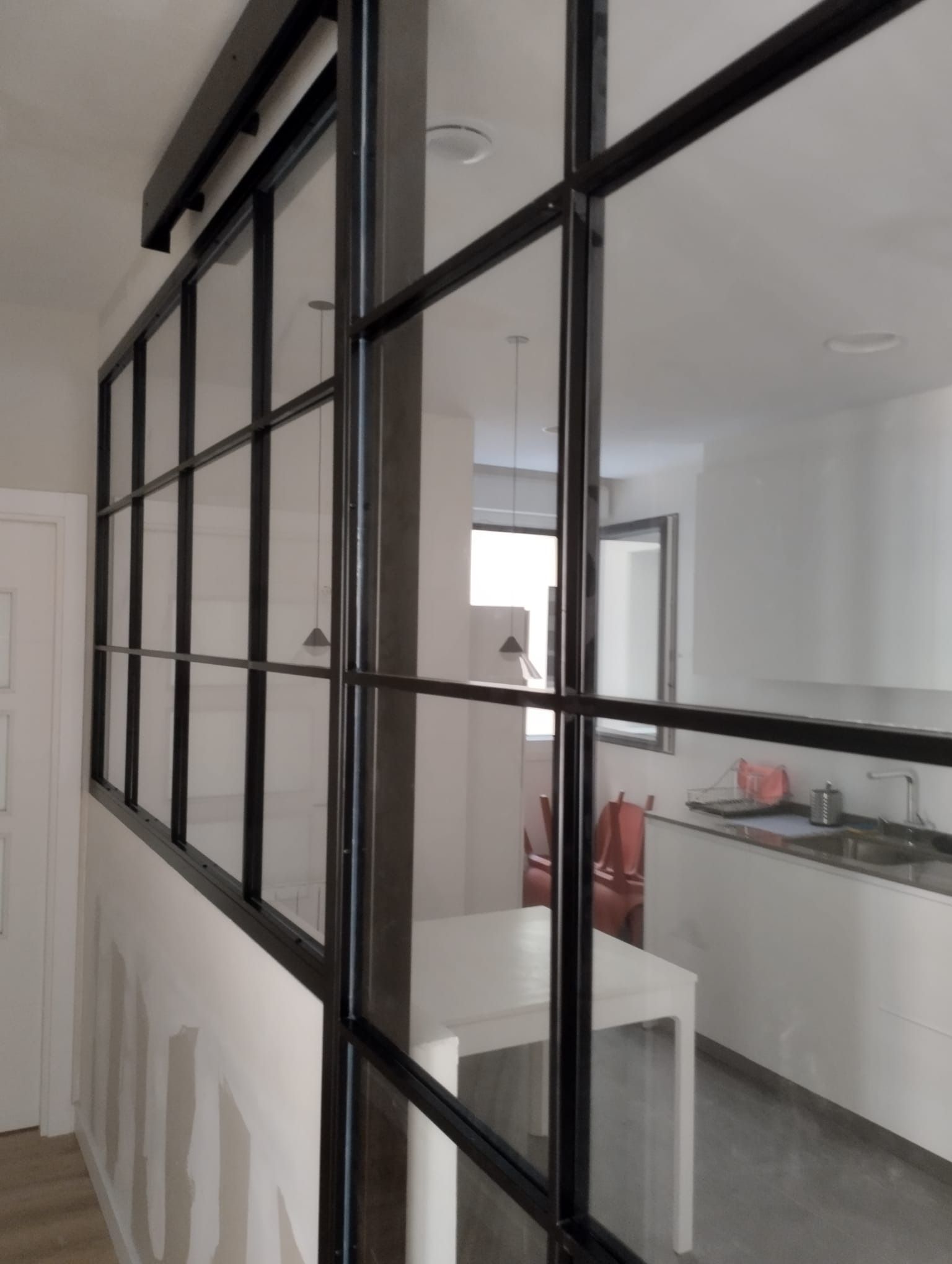 Una cocina con una mesa y sillas detrás de una pared de vidrio.
