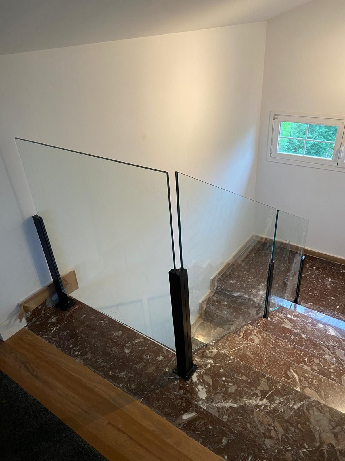 Una escalera con barandilla de cristal y una ventana.