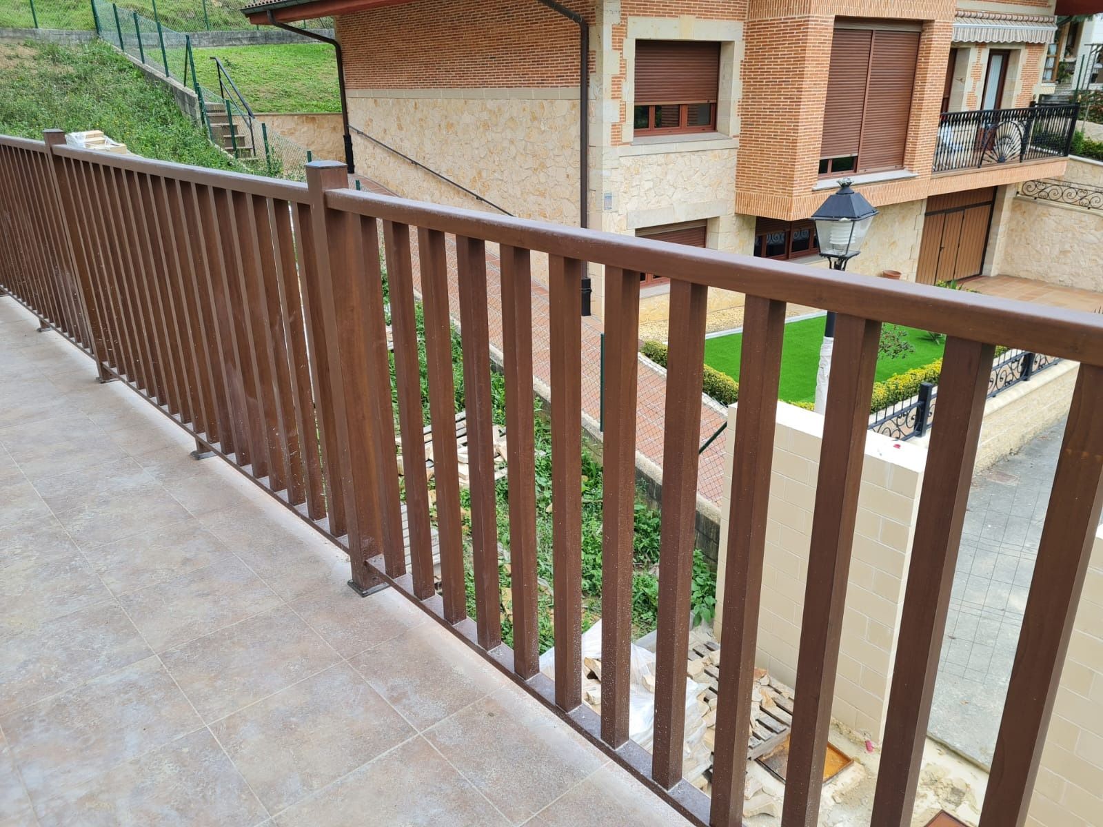 Un balcón con barandilla de madera y una casa al fondo.