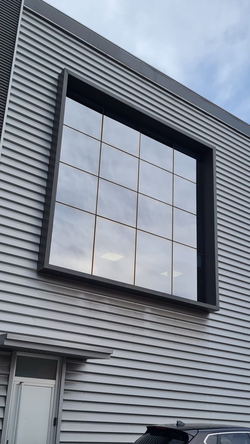 Una gran ventana en el lateral de un edificio con un coche aparcado delante.