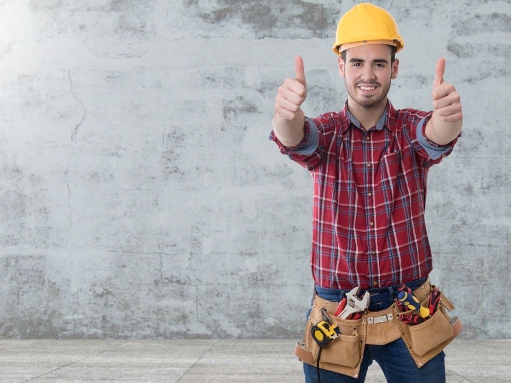 Un hombre que lleva un casco y un cinturón de herramientas está haciendo un gesto de aprobación con el pulgar hacia arriba.