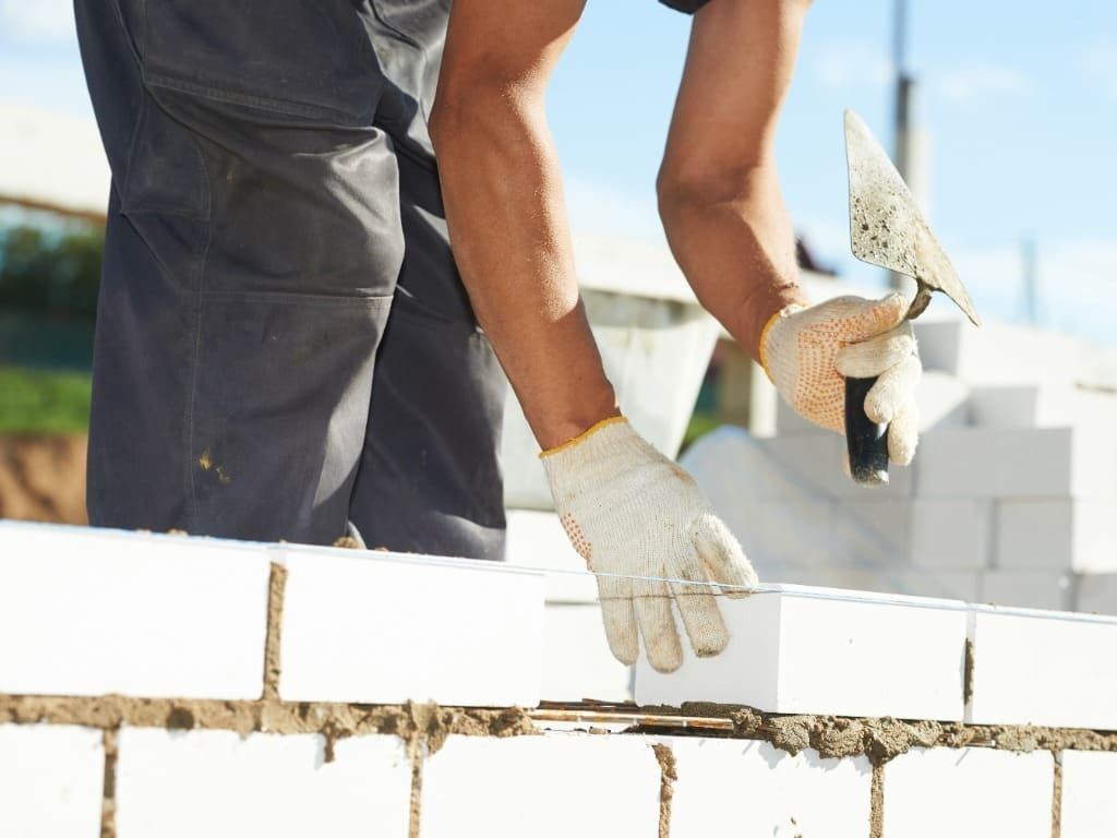 Un hombre está colocando ladrillos en una pared con una paleta.
