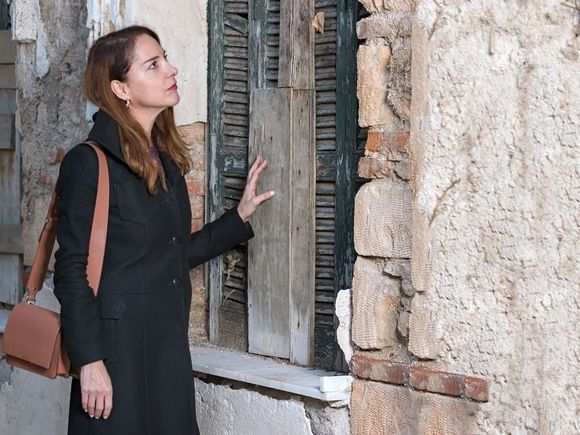 Una mujer con un abrigo negro está de pie junto a una ventana.