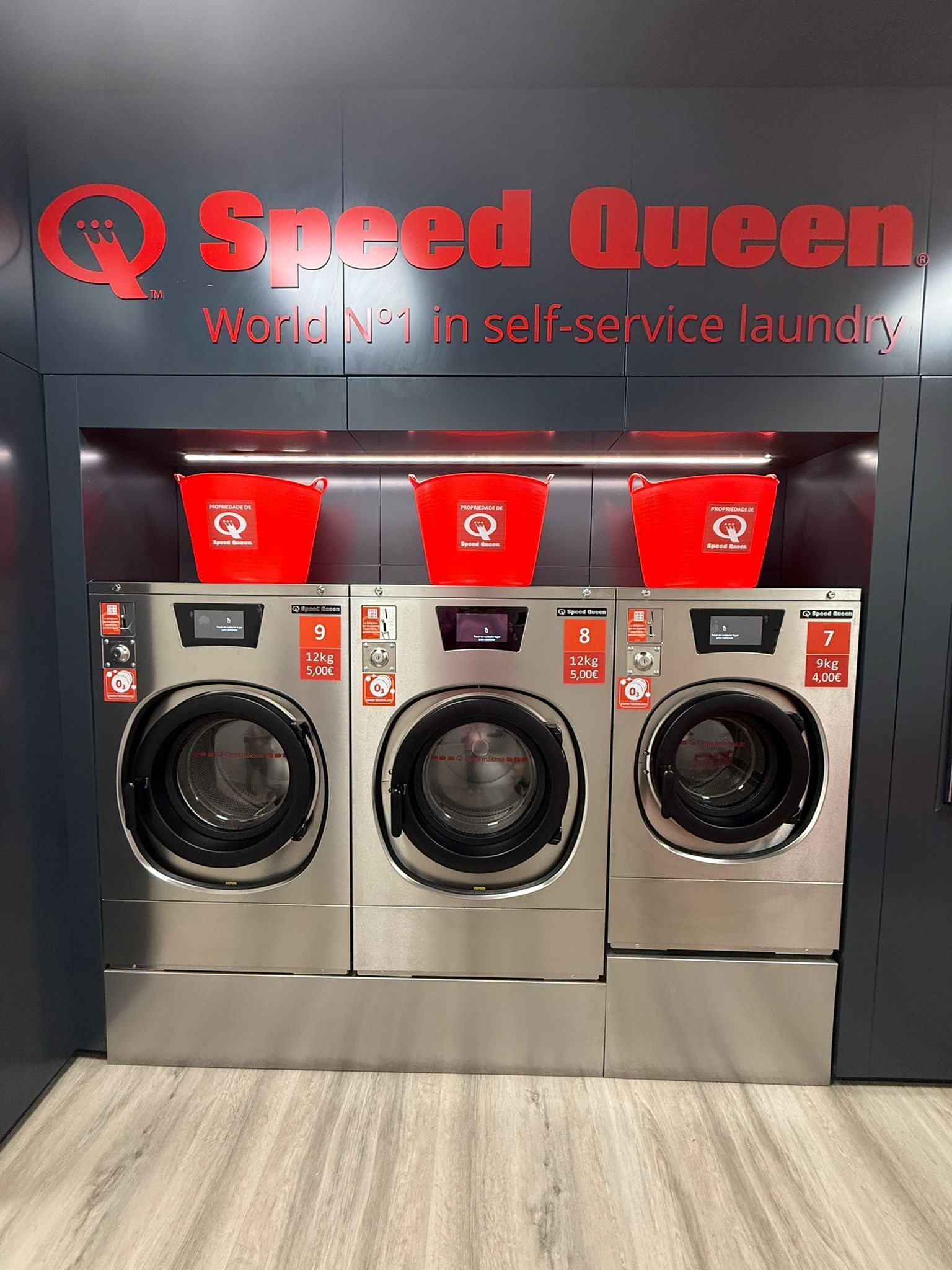 Una lavadora comercial de carga frontal, de color gris, con panel de control digital.