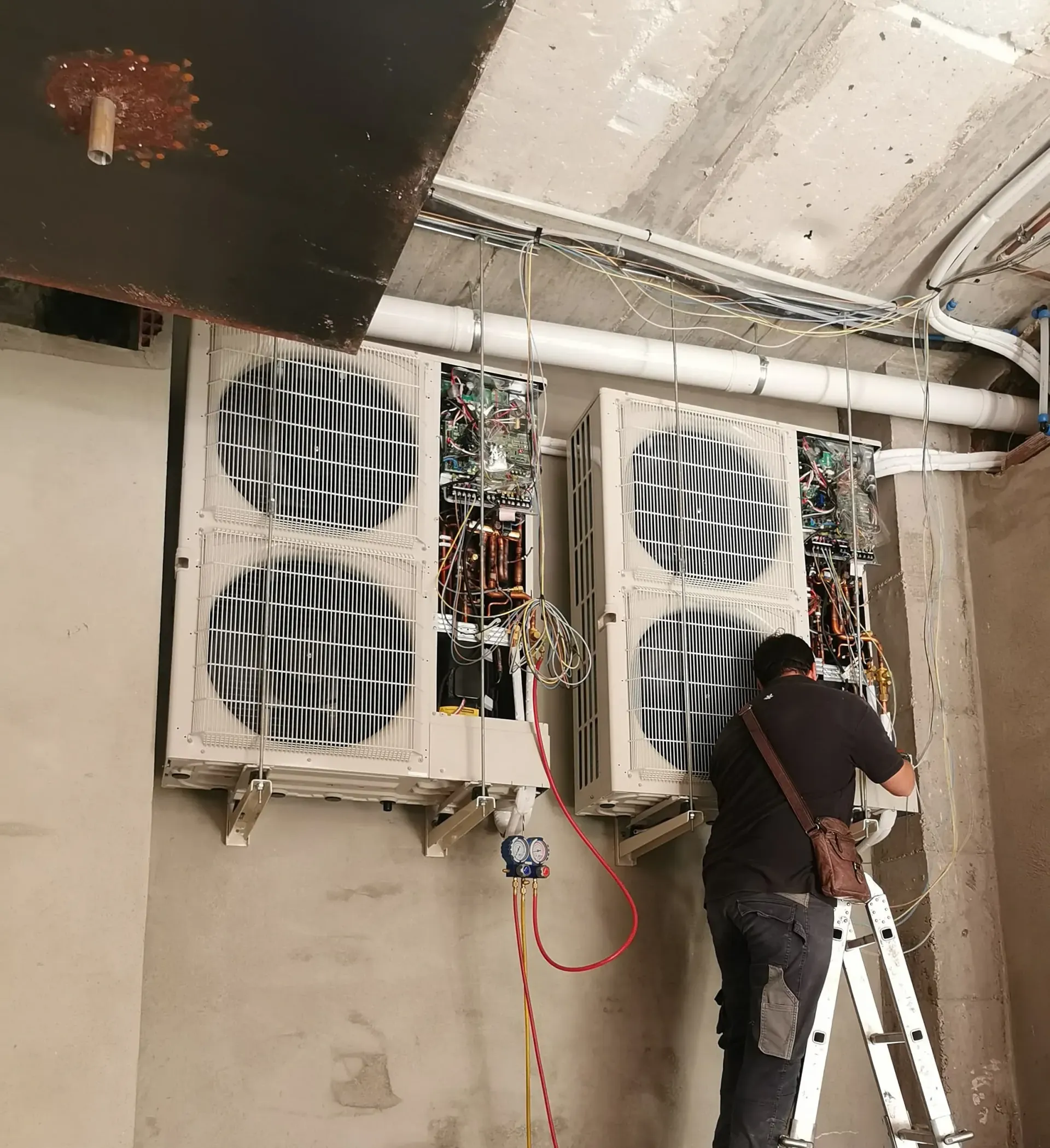 Un hombre está de pie en una escalera trabajando en un acondicionador de aire.