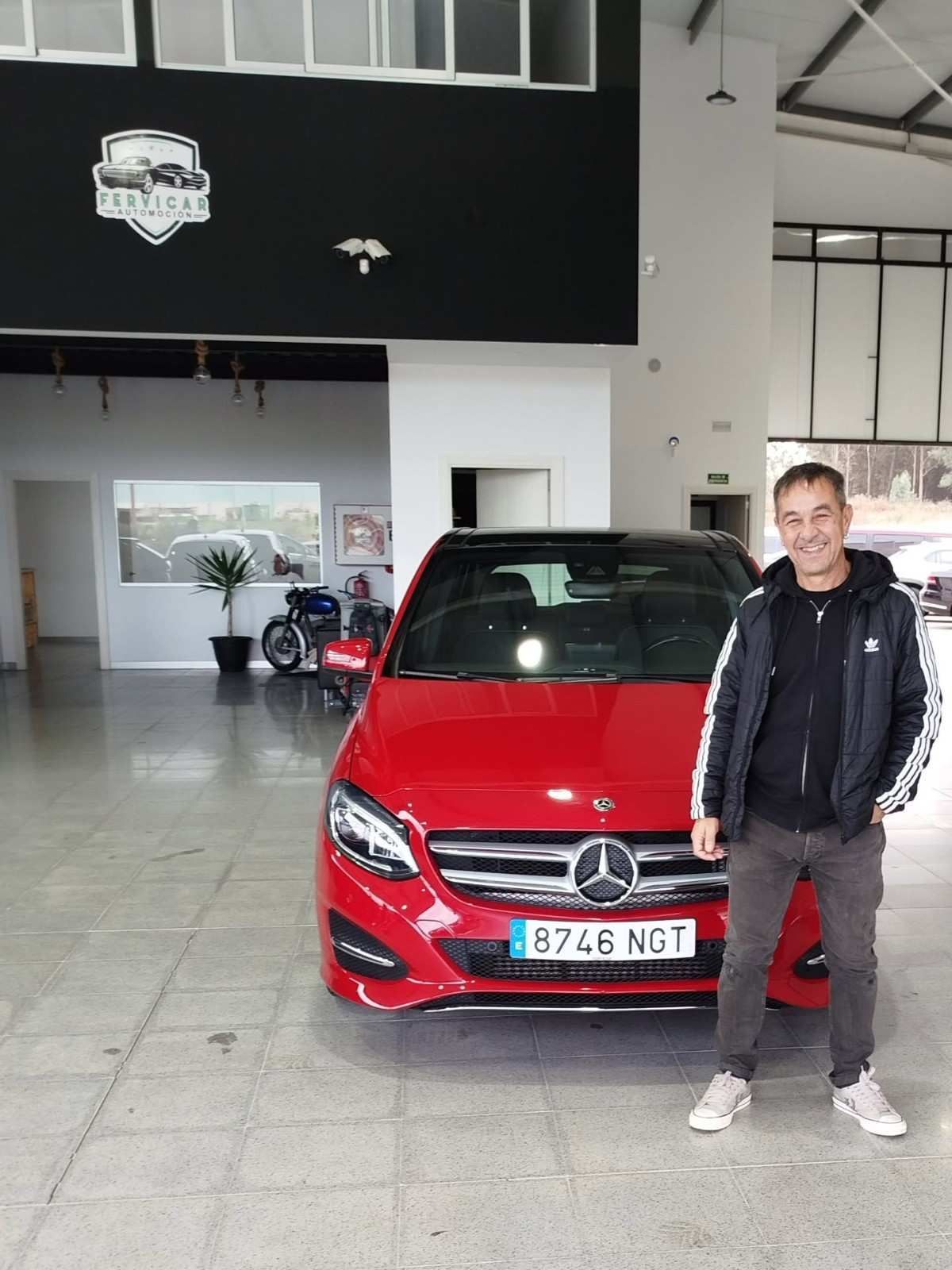 Un hombre de pie junto a un Mercedes rojo en un garaje que parece una sala de exposición.