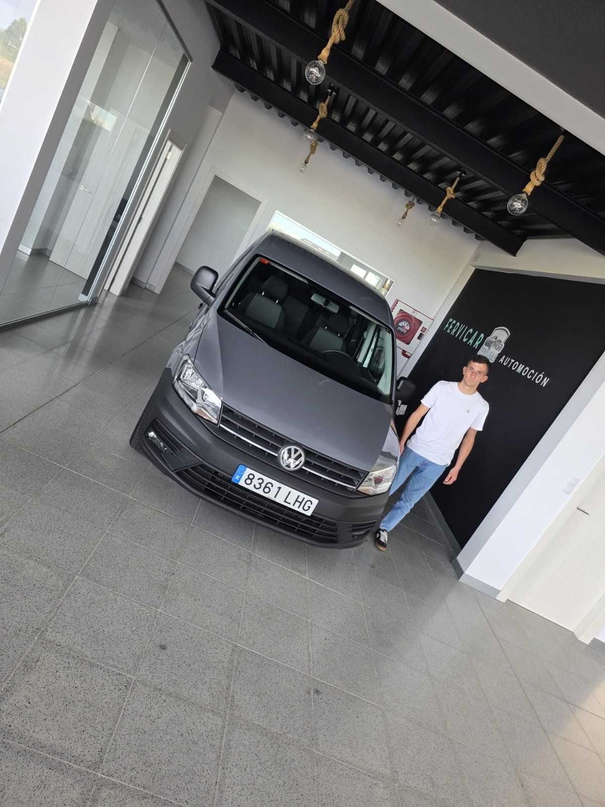 Un Volkswagen gris aparcado en el interior junto a un hombre con camisa blanca y vaqueros.