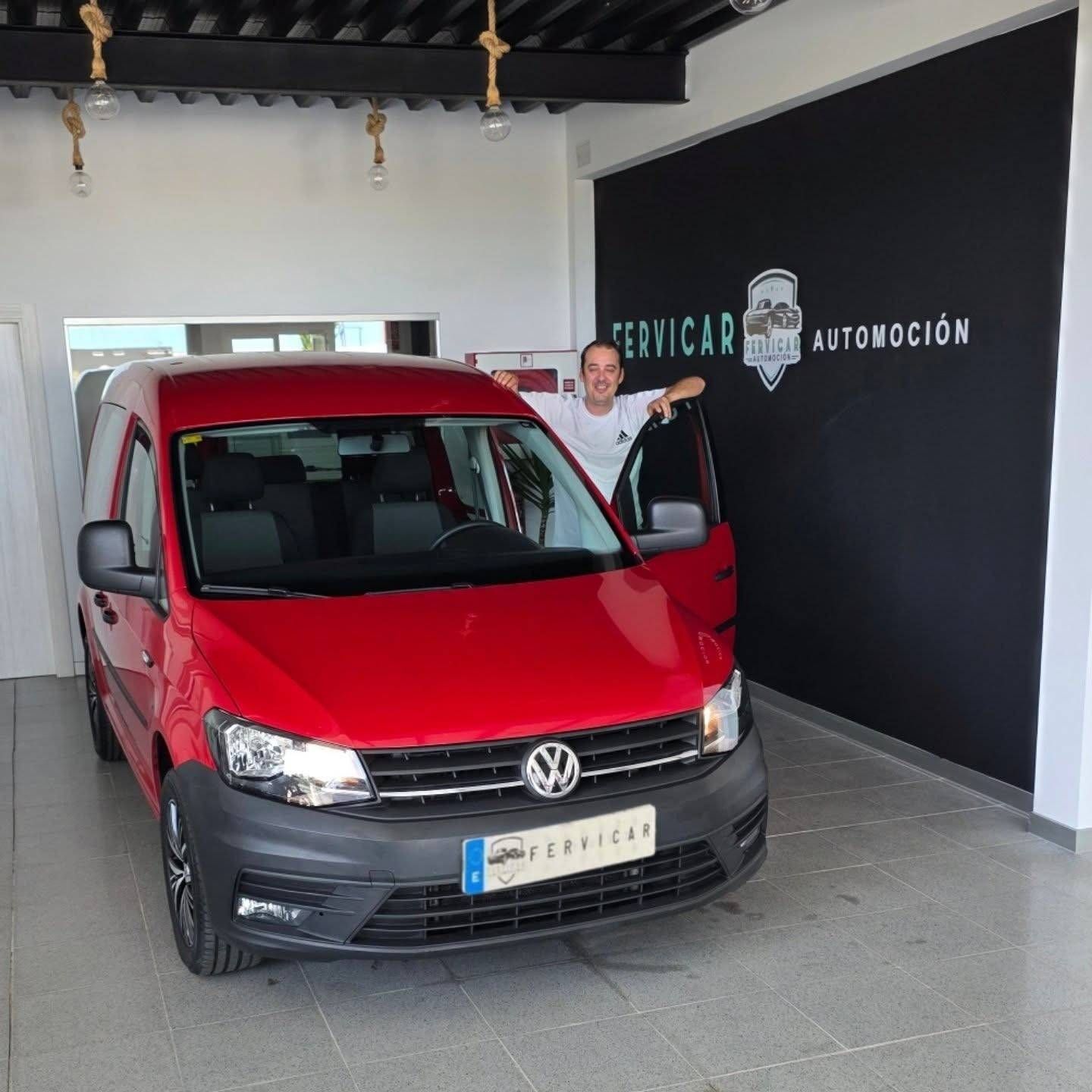 Una furgoneta Volkswagen roja en una sala de exposición, con un hombre de pie junto a ella, cerca de la entrada.