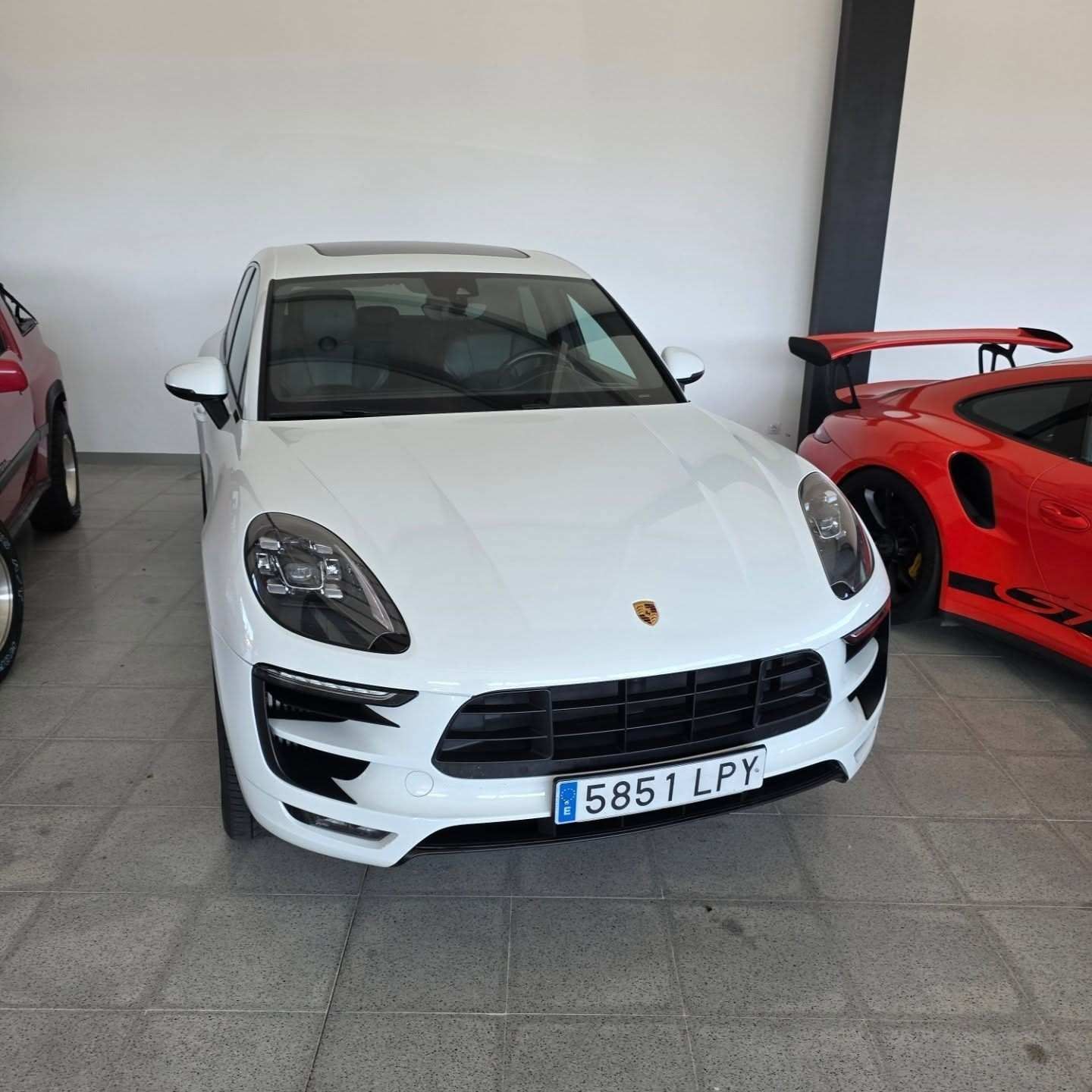 Un SUV Porsche blanco estacionado en el interior junto a un coche deportivo rojo.