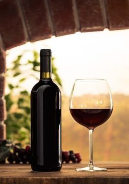 Una botella de vino tinto y una copa de vino tinto en una mesa de madera.