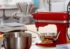 Una batidora roja está sobre una mesa al lado de una picadora de carne.