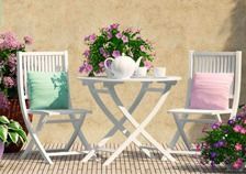 Una mesa y sillas en un patio con flores al fondo.