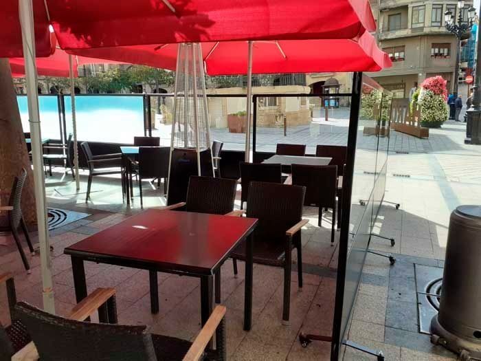 Un patio con mesas y sillas bajo sombrillas rojas.