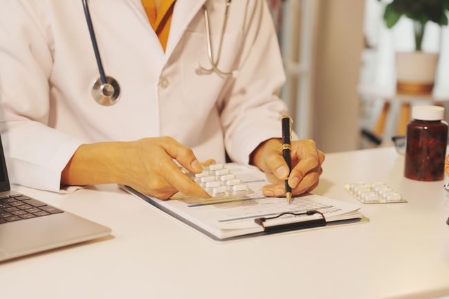 Un médecin rédige une ordonnance à son bureau, équipé d'un ordinateur portable, d'un stéthoscope et d'un flacon de médicament.