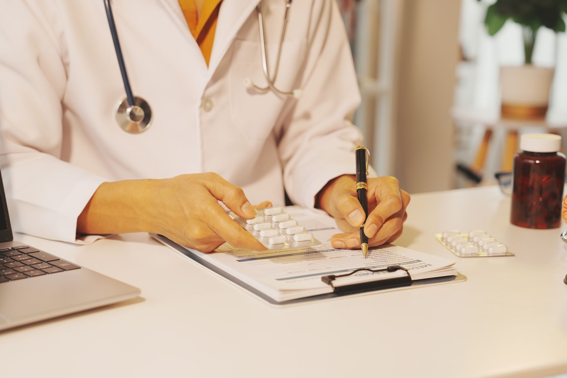 Un médecin rédige une ordonnance à son bureau, avec un ordinateur portable et des pilules.